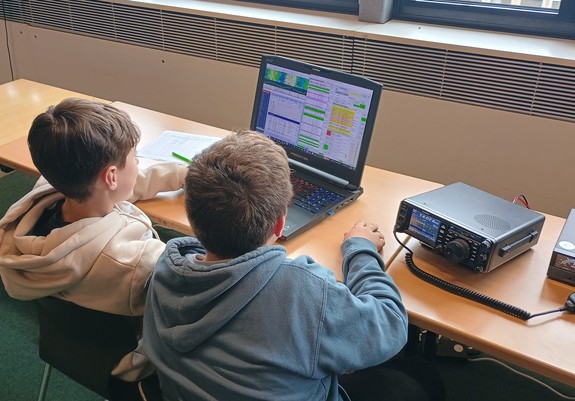 Zwei Schüler sitzen vor einem Laptop und einem Kurzwellentransceiver und betreiben FT8 auf 20m